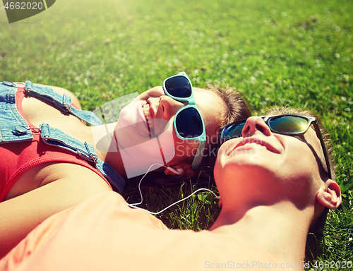 Image of happy teenage couple with earphones lying on grass