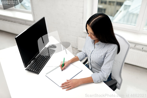 Image of businesswoman writing to notebook at office