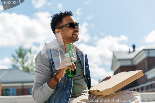 Image of indian man with pizza and drinking beer outdoors