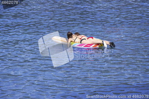 Image of Two young girls swimming on air mattress in the sea