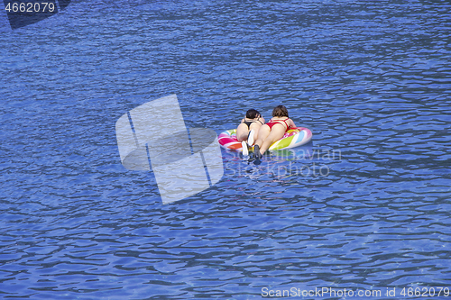 Image of Two young girls swimming on air mattress in the sea