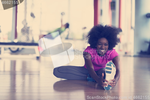 Image of woman in a gym stretching and warming up man in background worki