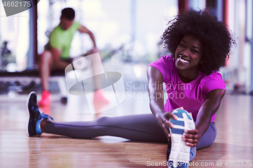 Image of woman in a gym stretching and warming up man in background worki