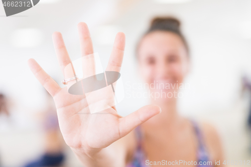 Image of Fit sporty active woman smiling, wearing fashion sportswear showing an open palm to the camera in yoga studio. Active urban lifestyle.