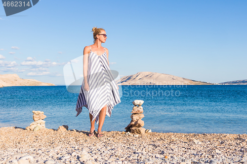 Image of Happy carefree woman enjoying late afternoon walk on white pabbled beach on Pag island, Croatia