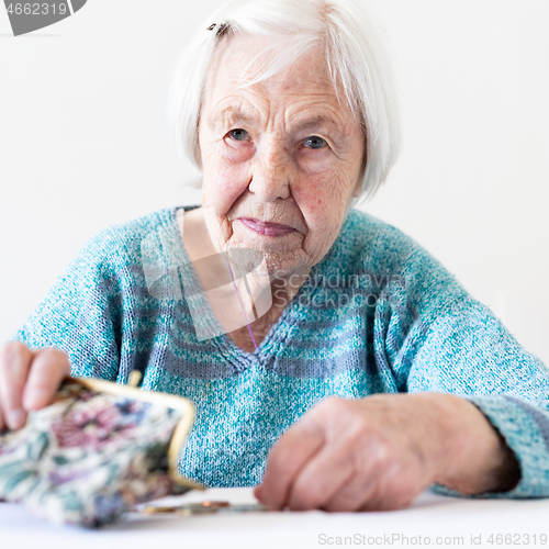 Image of Concerned elderly woman sitting at the table counting money in her wallet.