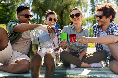 Image of happy friends drinking tea from thermos in summer