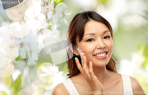 Image of young asian woman applying moisturizer to her face