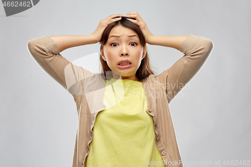 Image of terrified asian woman holding to her head