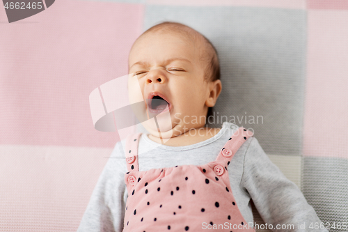 Image of yawning baby girl in pink suit lying on blanket