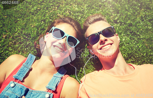 Image of happy teenage couple with earphones lying on grass