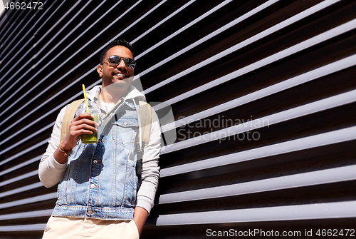 Image of man with backpack drinking smoothie on street