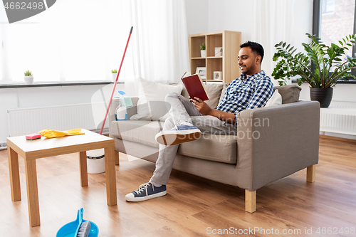 Image of man reading book and resting after home cleaning