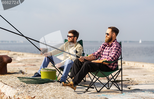 Image of male friends with fishing rods on sea pier