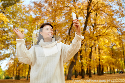 Image of woman taking selfie with smartphone at autumn park