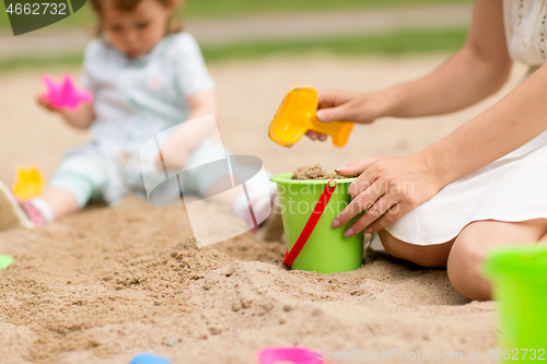 Image of mother playing with baby daughter in sandbox