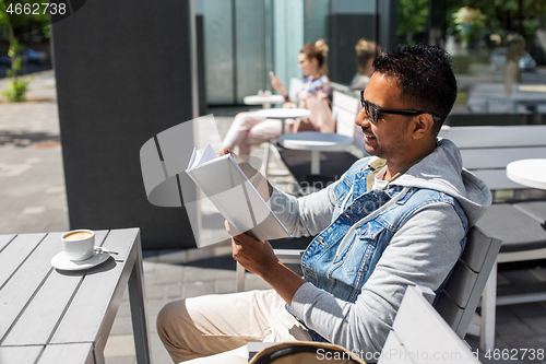 Image of indian man reading book at street cafe