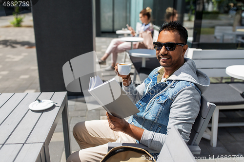 Image of man reading book and drinking coffee at city cafe