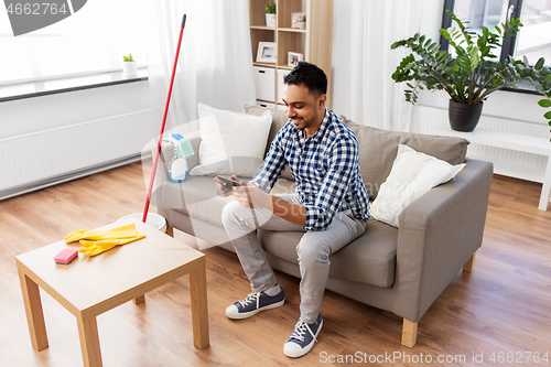 Image of man playing game on smartphone after cleaning home