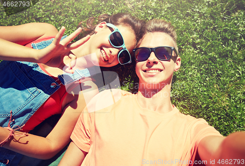 Image of happy teenage couple taking selfie on summer grass