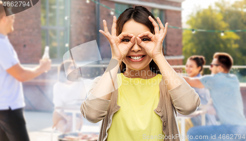 Image of asian woman making finger glasses at rooftop party