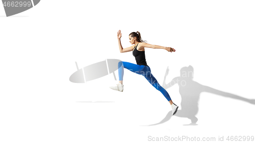 Image of Beautiful young female athlete stretching on white studio background with shadows