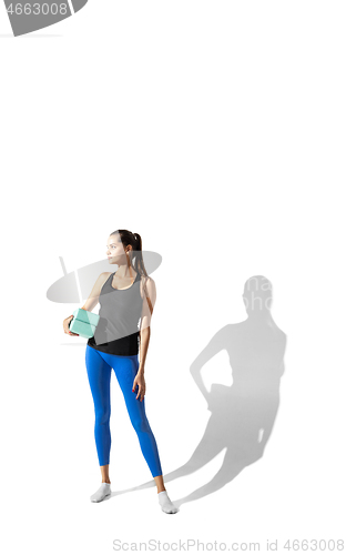 Image of Beautiful young female athlete stretching on white studio background with shadows