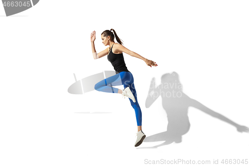 Image of Beautiful young female athlete stretching on white studio background with shadows