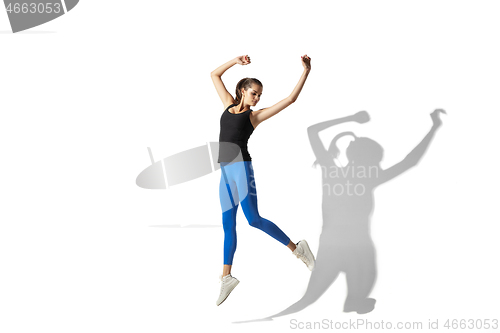 Image of Beautiful young female athlete stretching on white studio background with shadows