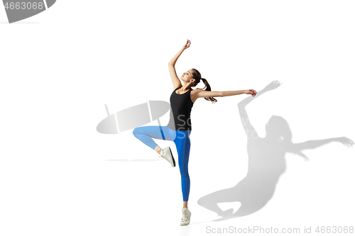 Image of Beautiful young female athlete stretching on white studio background with shadows