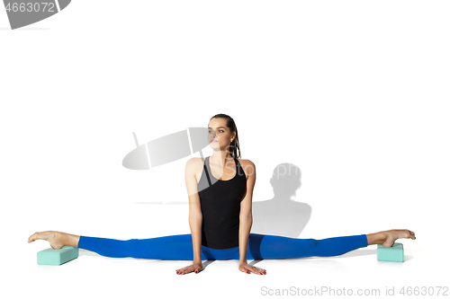 Image of Beautiful young female athlete stretching on white studio background with shadows