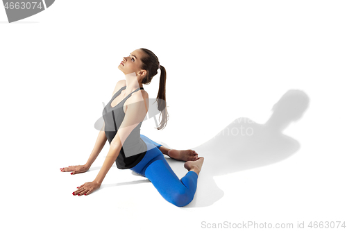 Image of Beautiful young female athlete stretching on white studio background with shadows