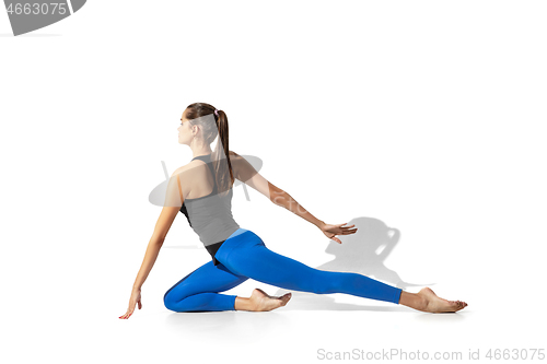 Image of Beautiful young female athlete stretching on white studio background with shadows