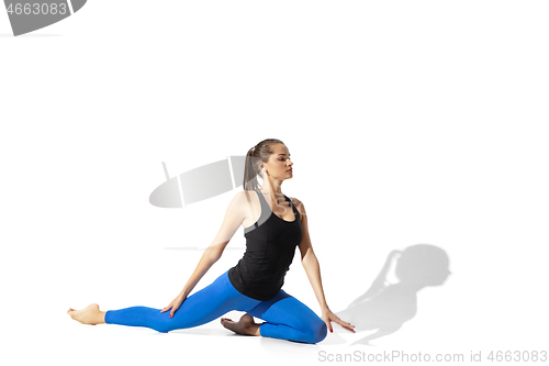 Image of Beautiful young female athlete stretching on white studio background with shadows