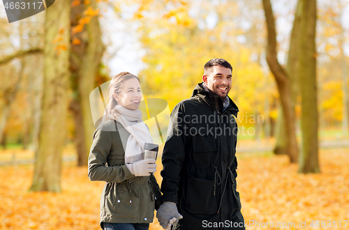 Image of couple with tumbler walking along autumn park