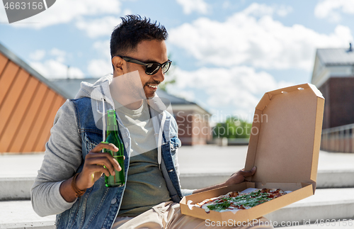 Image of indian man with pizza and drinking beer outdoors