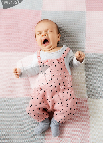 Image of yawning baby girl in pink suit lying on blanket