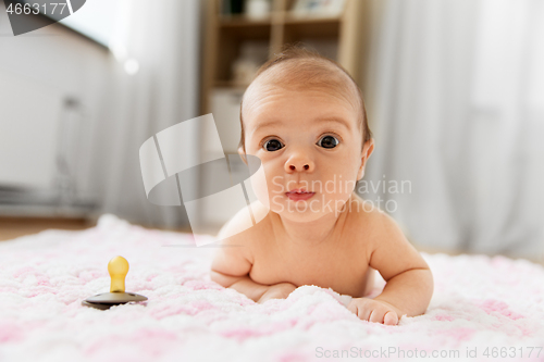 Image of baby girl in diaper lying with pacifier on blanket