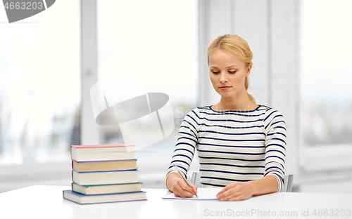 Image of student woman with books writing to notebook