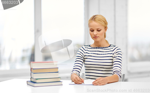Image of student woman with books writing to notebook