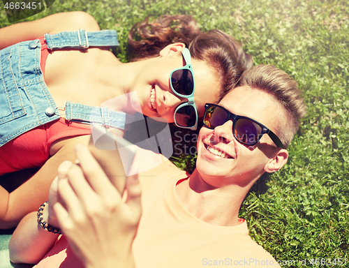 Image of happy teenage couple smartphone lying on grass