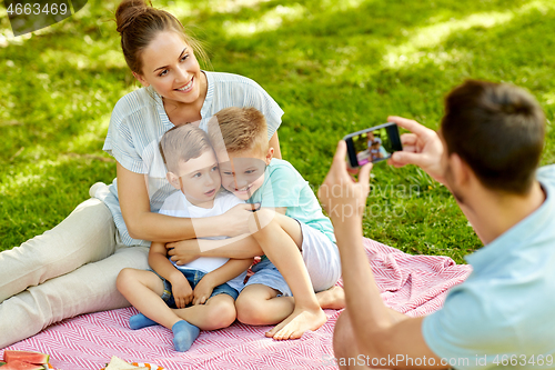 Image of father taking picture of family on picnic at park