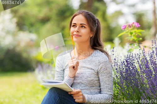 Image of young woman writing to notebook at summer garden