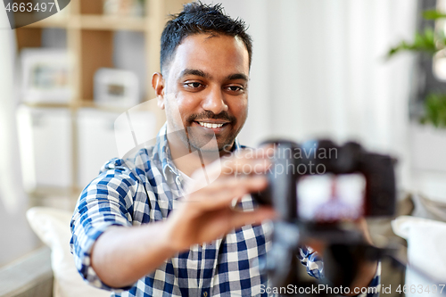 Image of indian male video blogger adjusting camera at home