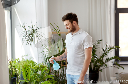 Image of man spraying houseplants with water at home