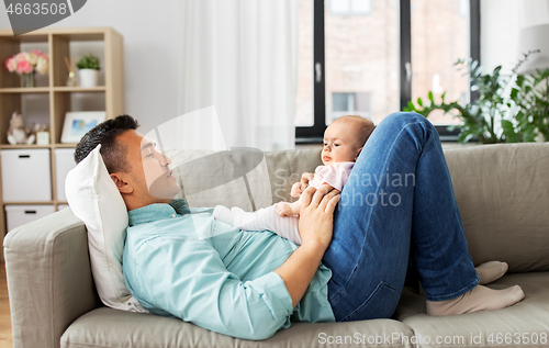 Image of middle aged father with baby lying on sofa at home