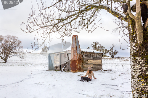 Image of Woman relaxing in snowy field with old rustic barn