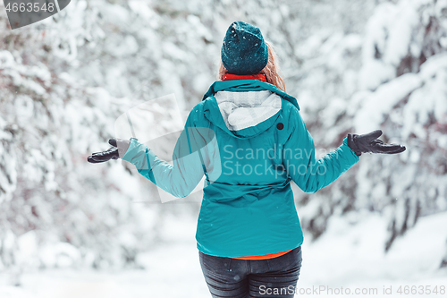 Image of Woman standing in snow among pine forest with snow falling