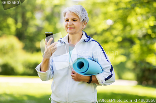 Image of old woman with exercise mat and smartphone at park