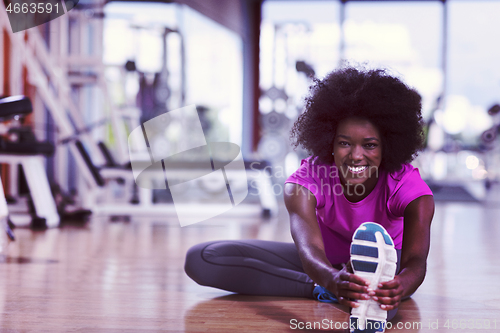 Image of woman in a gym stretching and warming up man in background worki